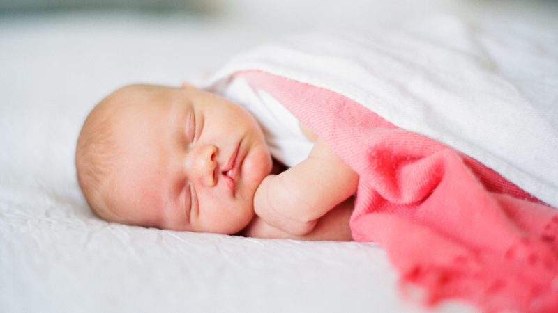 Newborn baby boy with cleft lip sleeping on a bed in a pink ombre blanket